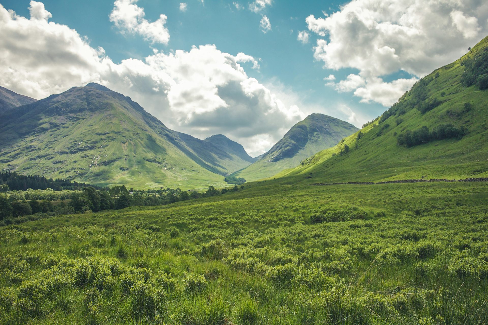 A green valley between mountains under a blue sky with white clouds in Scotland